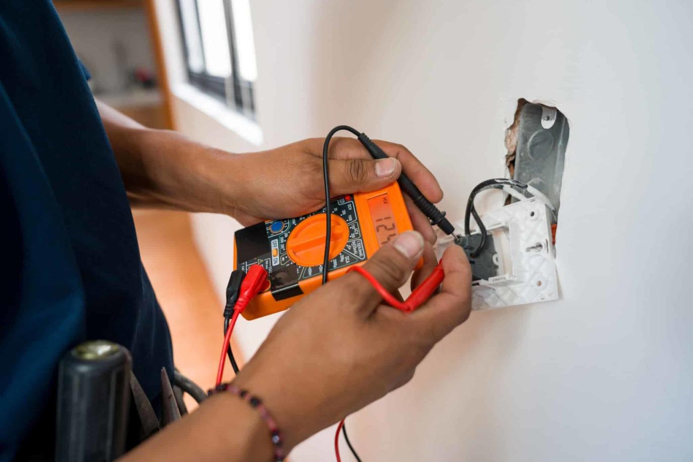 En elektriker bruger et multimeter til at teste en stikkontakt på en væg.
