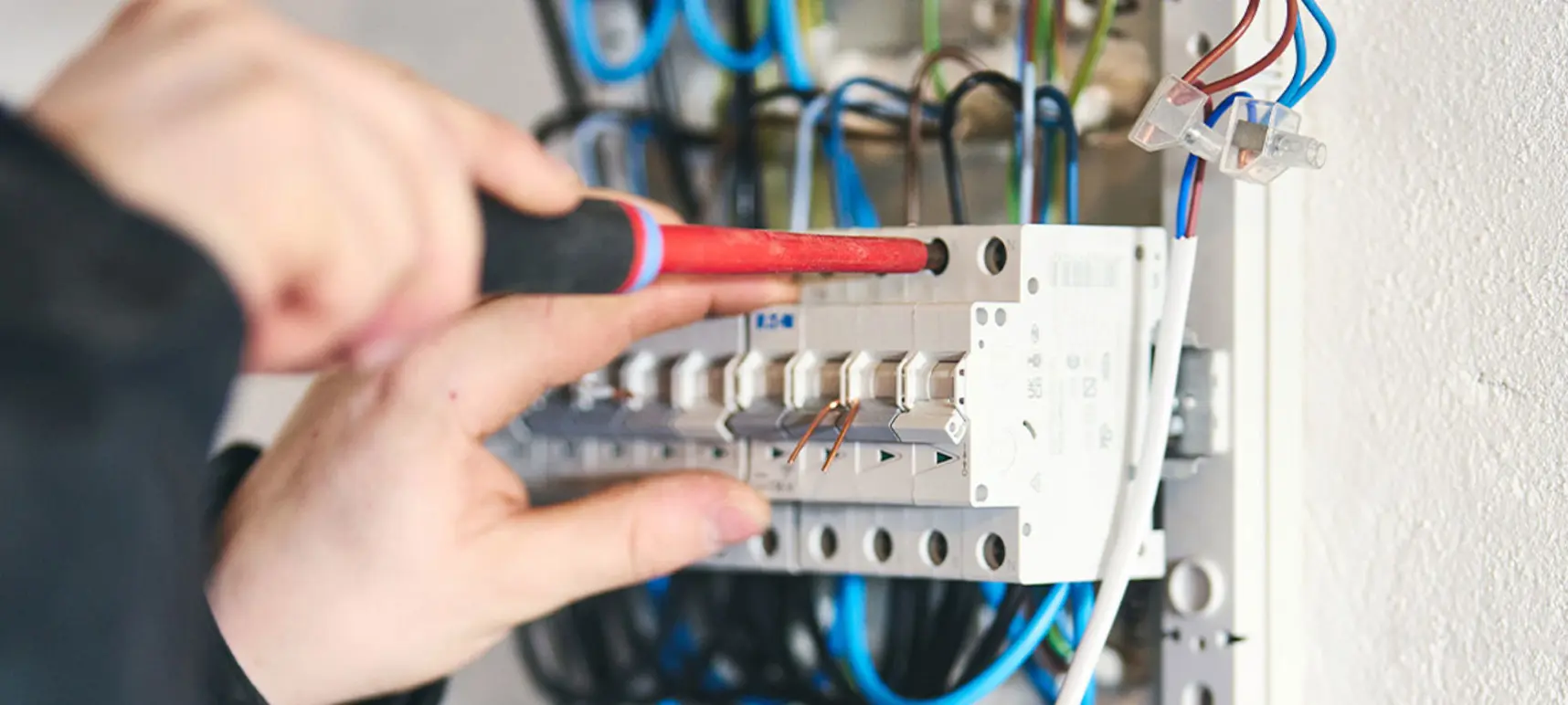 En hånd bruger en skruetrækker til at arbejde på en elektrisk tavle med ledninger.