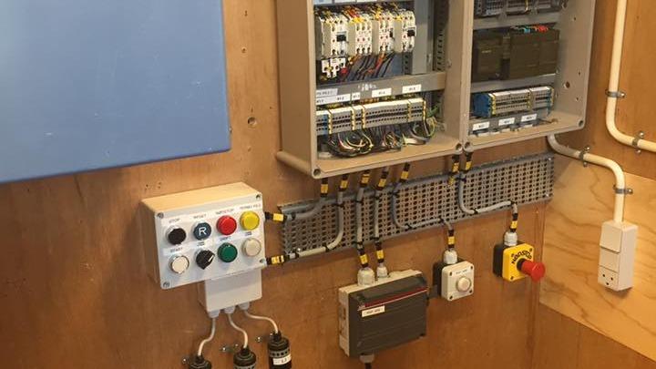 Billede af en elektrisk tavle med ledninger, kontakter og styringspanel på en væg.