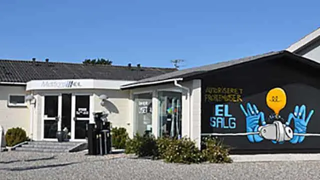 Butik med moderne facade og farverig vægmaleri, der reklamerer for el-salg. Grusbelagt indkørsel foran.