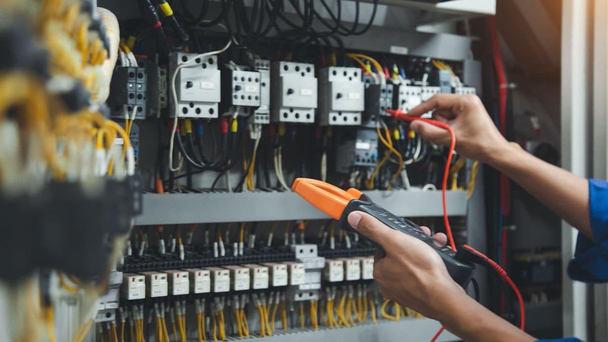 En person bruger en multimeter til at teste elektriske forbindelser i et kontrolpanel.