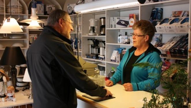 En mand taler med en kvinde bag disken i en butik med køkkenudstyr og lamper.