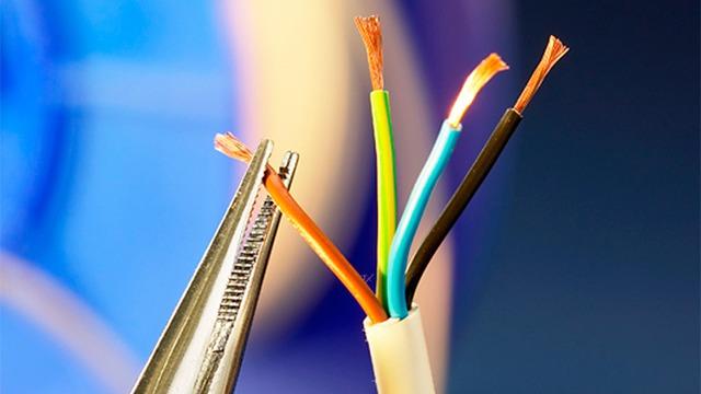 Nærbillede af en ledningsskærer, der holder en elektrisk ledning med farvede ledninger.