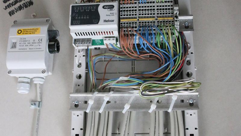 Billede af en elektrisk tavle med ledninger, relæer og en strømforsyning monteret på en metalplade.