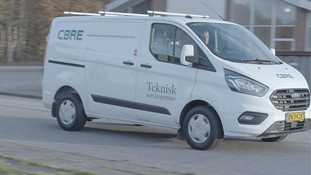 En hvid varevogn fra CBRE med teksten "Teknisk inspektion" kører på en vej.
