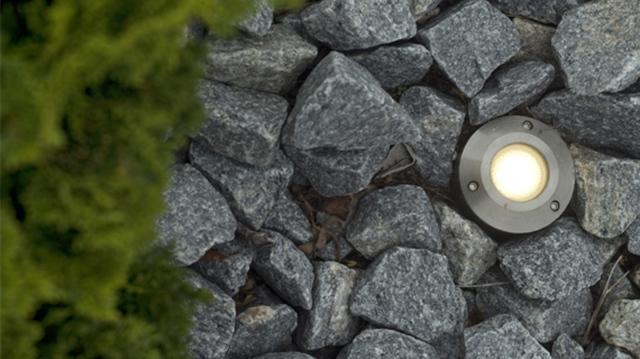 Indbygget havebelysning i grå sten med grønne planter i nærheden, der skaber en hyggelig atmosfære.