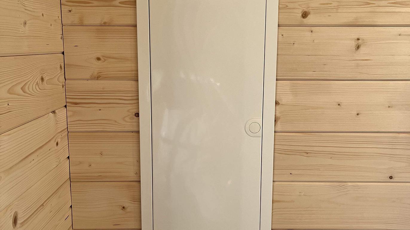 Hvid dør på en væg af lyst træpanel i et rum med naturlig belysning.