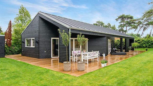 Moderne sort hus med træterrasse og havemøbler i en grøn have.