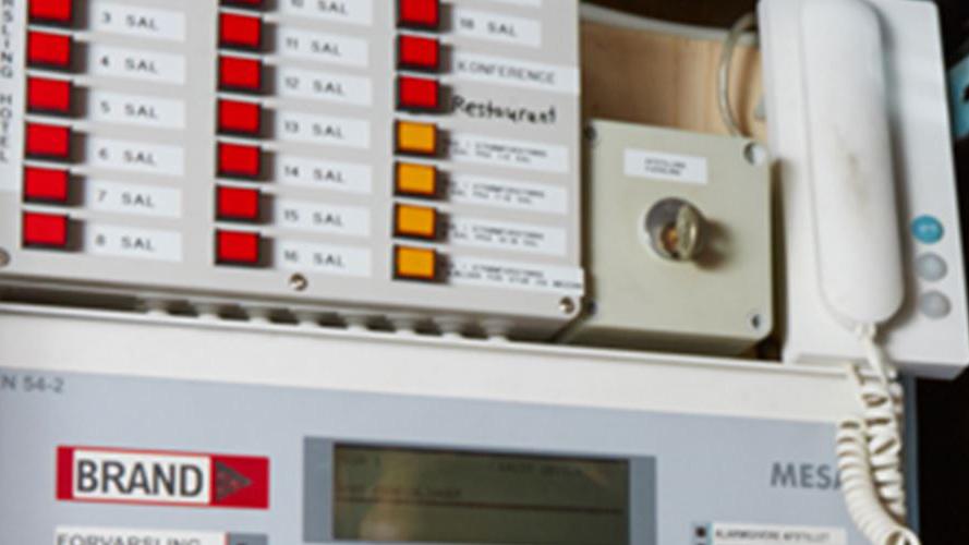 Brandalarmsystem med knapper og telefon, der viser status for brandalarmer i bygningen.