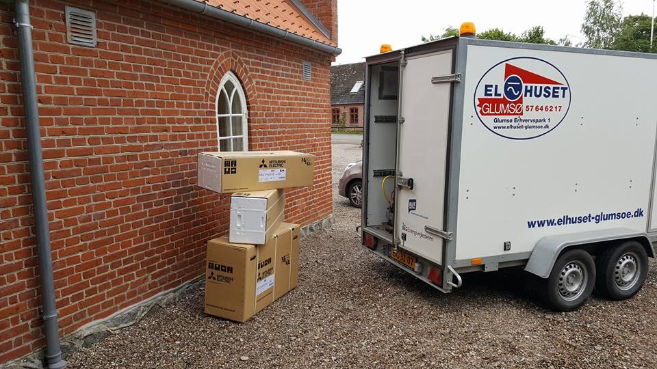 Kasser stablet ved en murstensvæg ved siden af en trailer med logoet fra Elhuset.