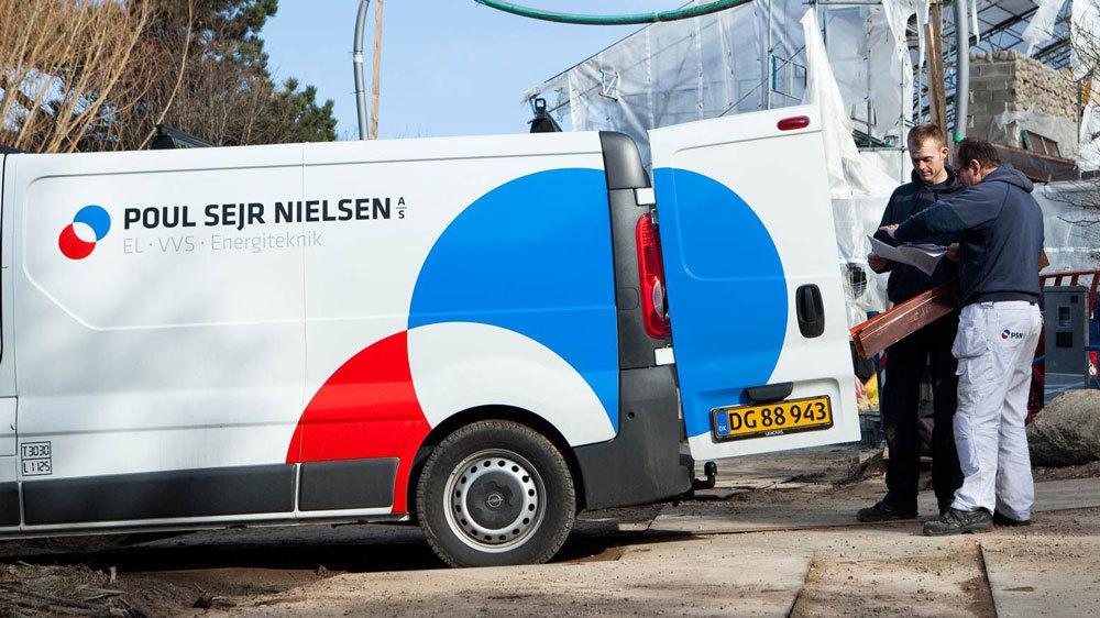 To personer, der arbejder ved en hvid varevogn fra Poul Sejr Nielsen, med materialer og værktøj.