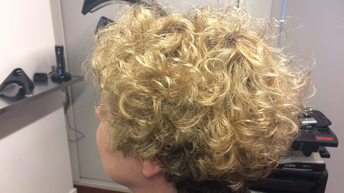 En person med krøllet, blond hår set fra siden i en frisørsalon.
