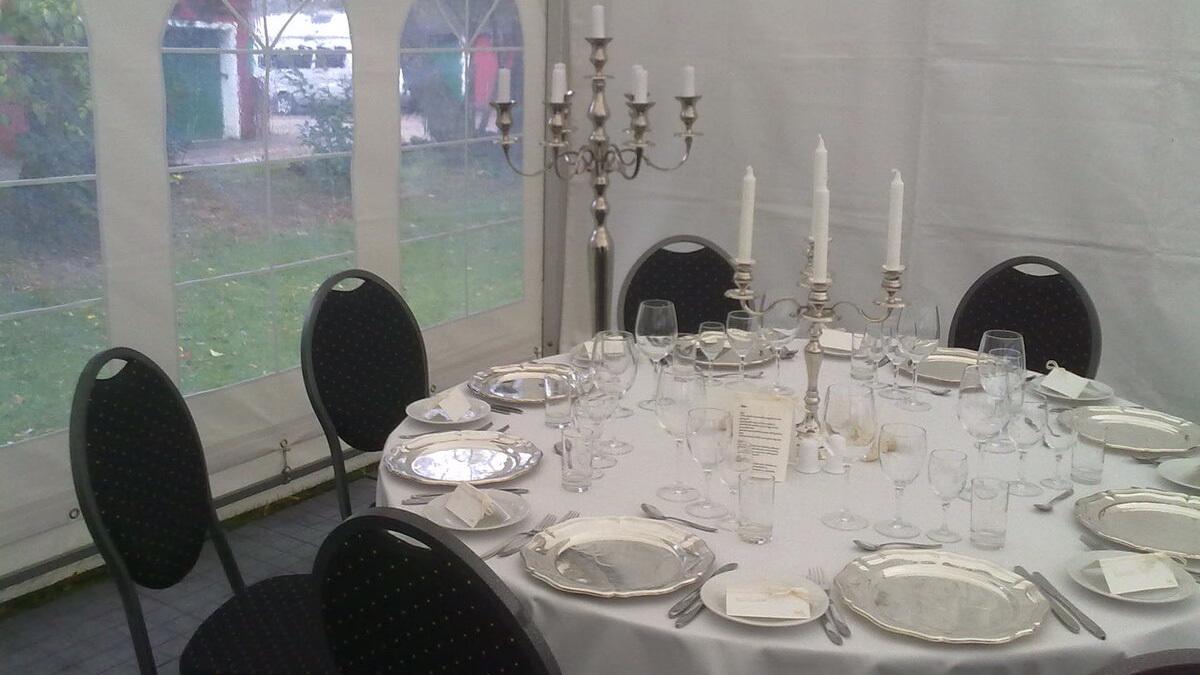 Elegant dækket bord med sølvbestik, glas og stearinlys i en teltlignende opstilling.