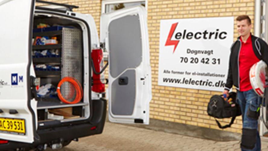 En mand står ved siden af en hvid varevogn med værktøj og udstyr, klar til at udføre el-installationer.