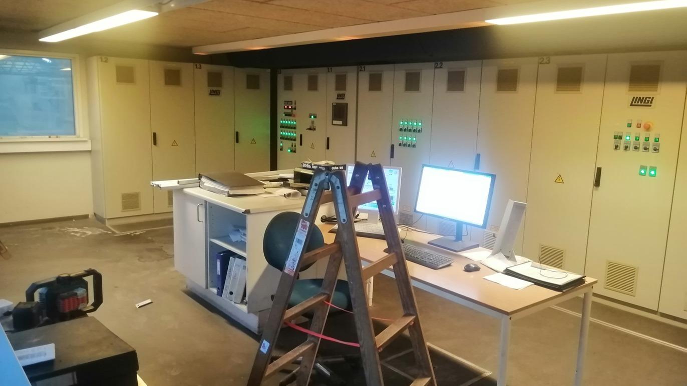 Et kontor med en computer, en stige og flere skabe med lysindikatorer på væggen.