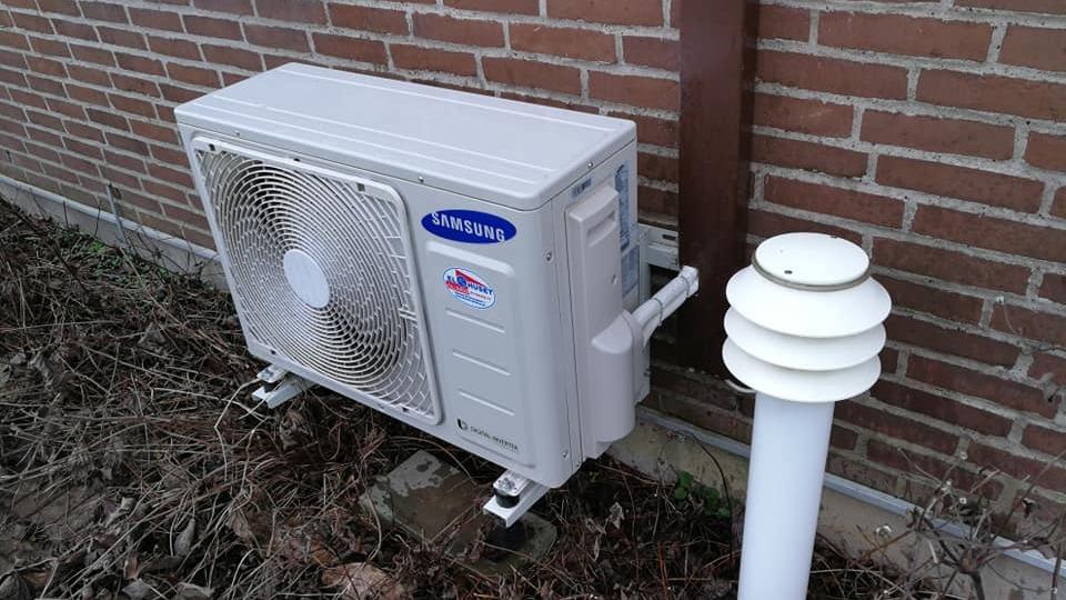 Udendørs klimaanlæg monteret på mur med ventilationsrør og skorstenslignende udluftning.