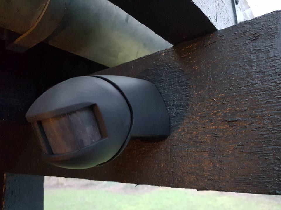 Bevægelsessensor monteret på en sort træbjælke under en tagudhæng.