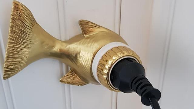 En gylden fiskekontakt med en stikkontakt tilsluttet, monteret på en hvid væg.
