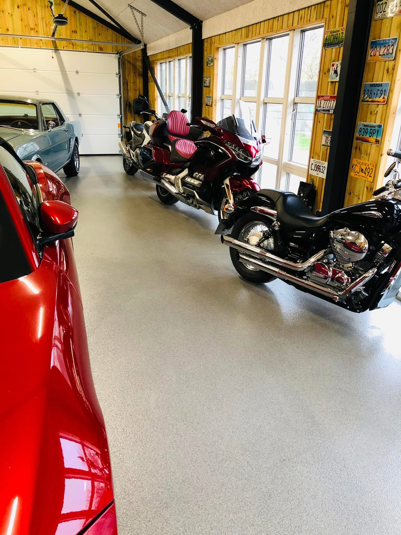 En rummelig garage med en rød bil, to motorcykler og en garageport i baggrunden.