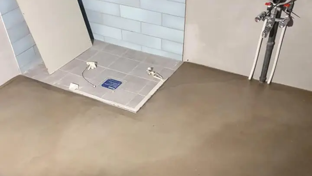 Billede af et rum med ny betonbund, fliser og installationer til vand og elektricitet.