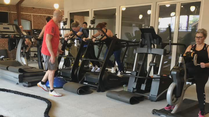Trænende personer i et fitnesscenter med forskellige træningsmaskiner og udstyr.