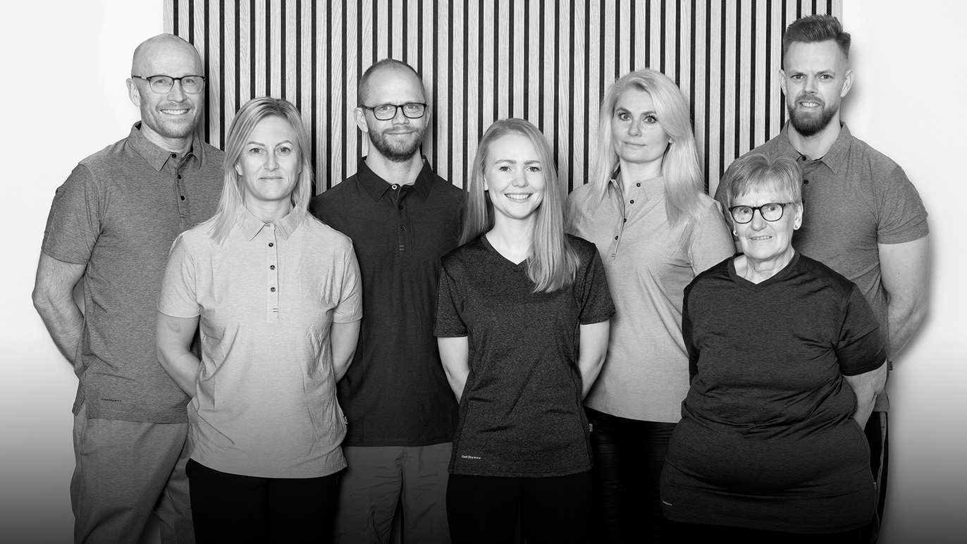 Syv personer står sammen foran en stribet baggrund, iført grå poloer og smiler til kameraet.
