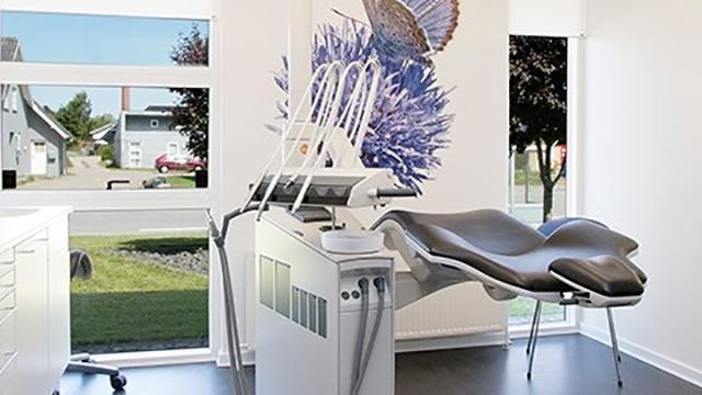 Moderne tandlægeklinik med en tandlægestol og udstyr, samt en vægdekoration af en sommerfugl.