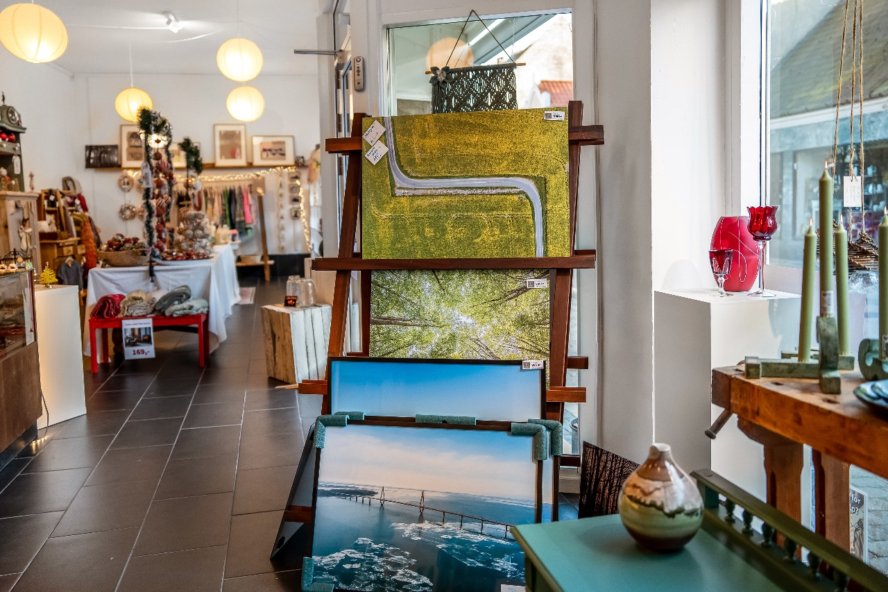 Indendørs kunstbutik med malerier på staffeli og dekorationer i baggrunden.