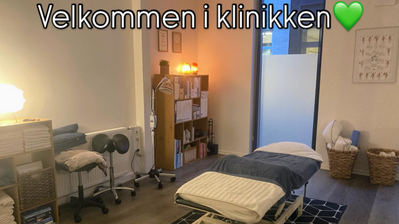 Behandlingsrum i klinikken med massagebriks, hylder og velkomstskilt.