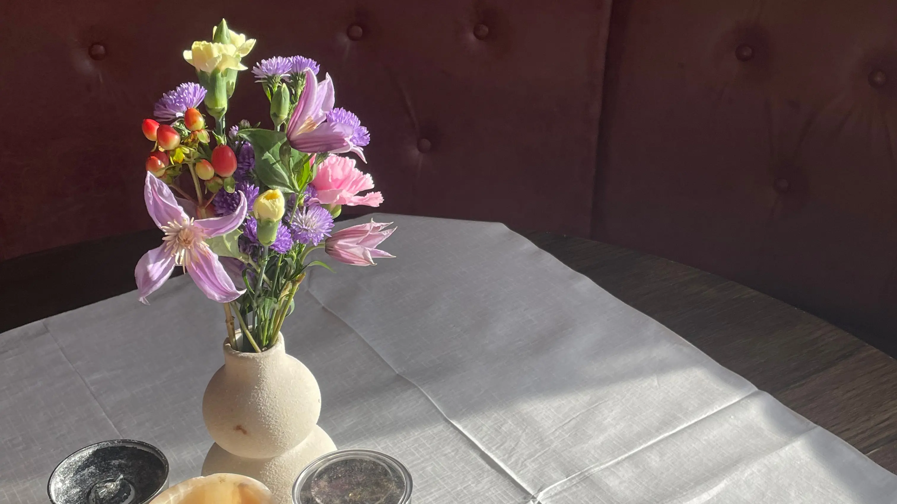 En vase med farverige blomster står på et bord dækket med en hvid dug, omgivet af små skåle.