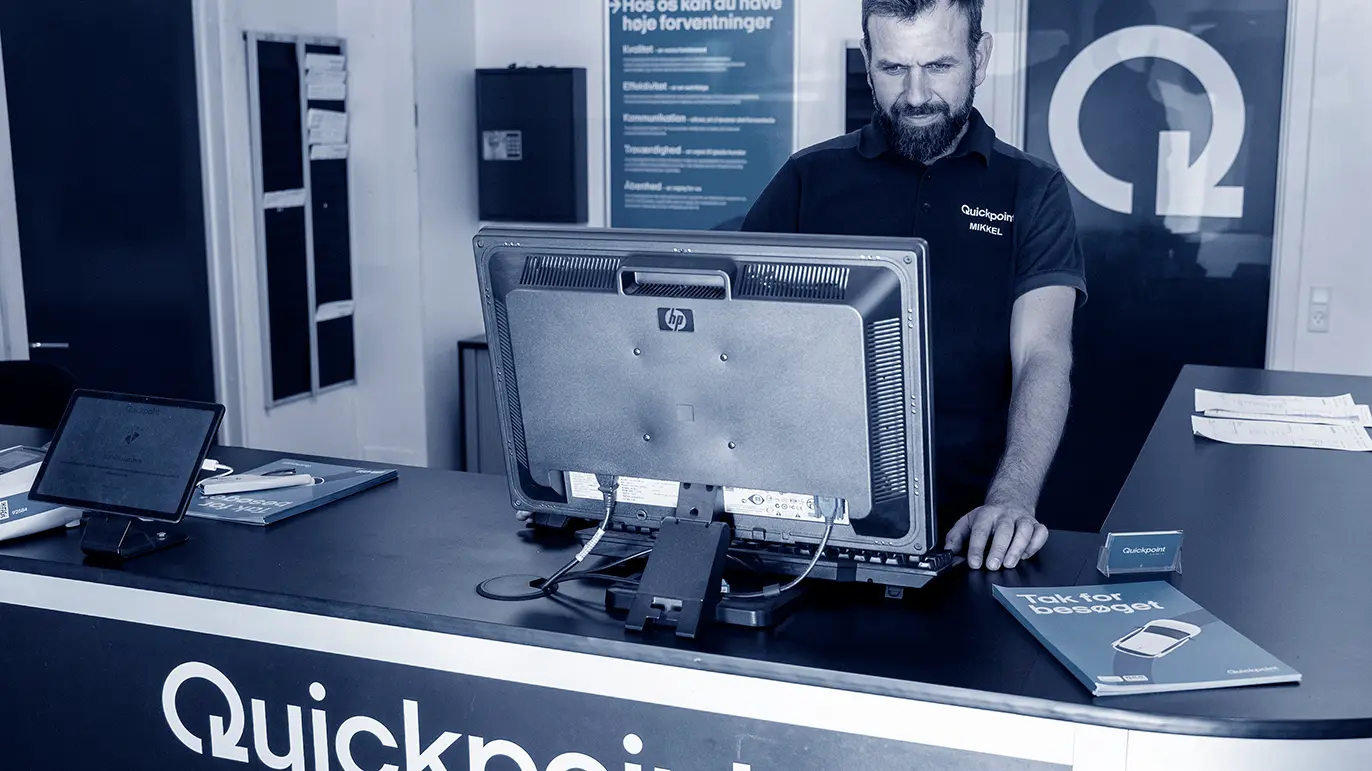En mand står ved en reception med en computer og brochurer fra Quickpoint.