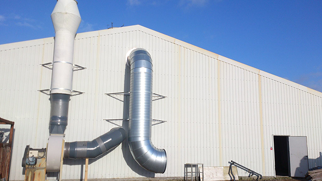 Metalrør og ventilationssystem på en industriel bygning under en blå himmel.