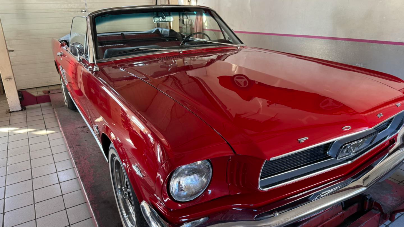 En rød klassisk Ford Mustang cabriolet parkeret i en garage med fliser på gulvet.