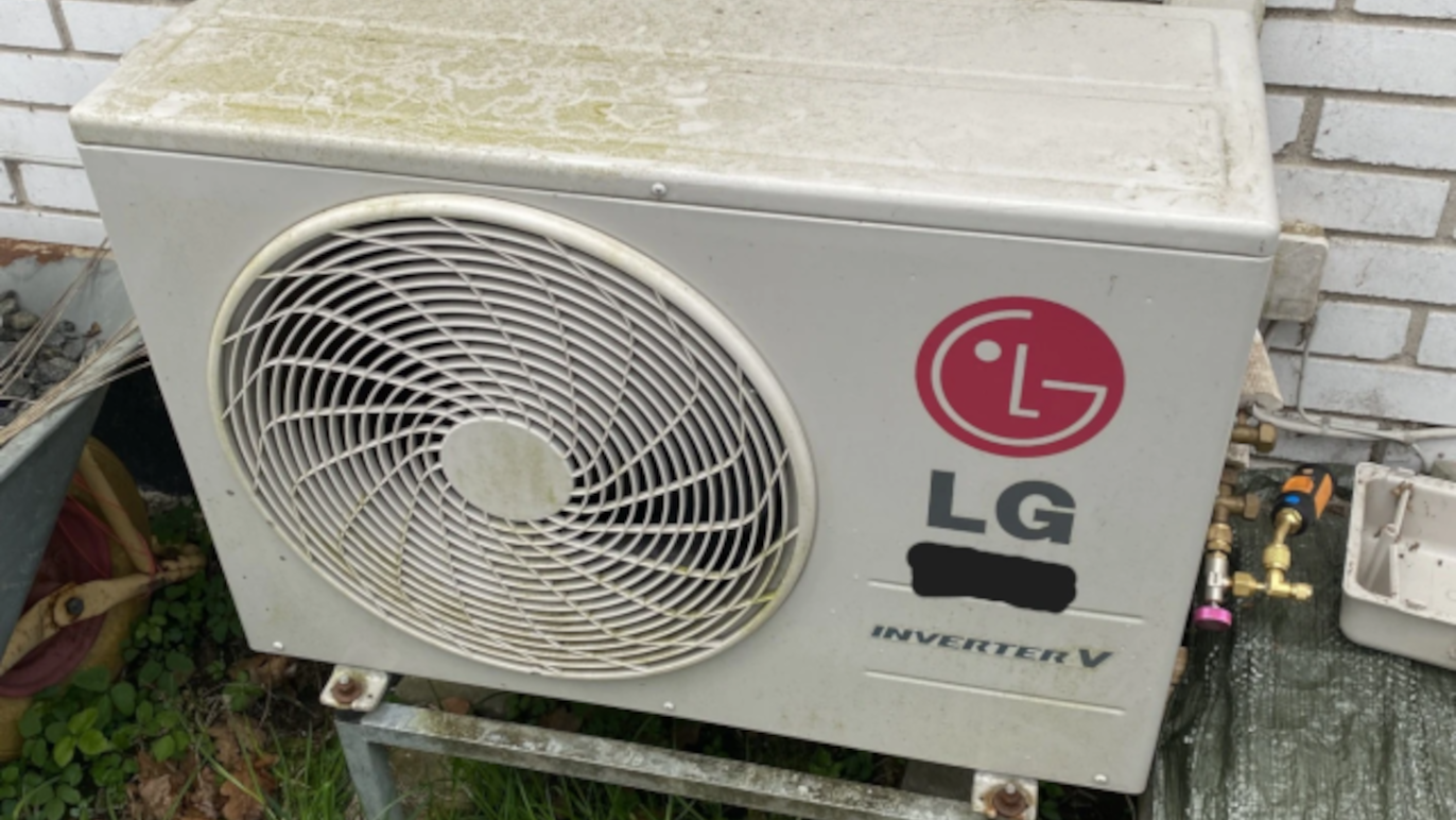 Udendørs airconditionanlæg fra LG med inverterteknologi, placeret på en metalramme ved en mur.