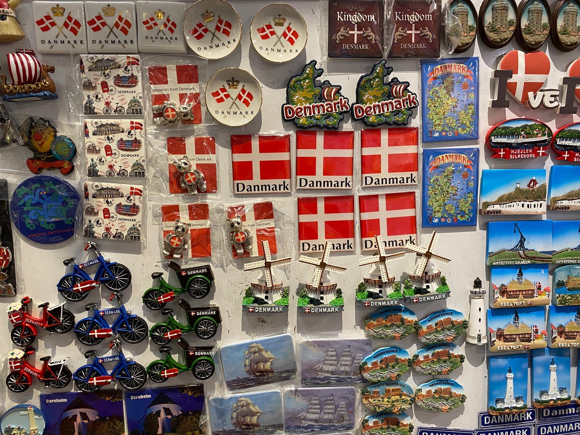 En væg fyldt med souvenirs fra Danmark, herunder magneter, postkort og små modeller af cykler og vindmøller.