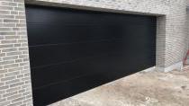 En moderne sort garageport i en murstensvæg, der står åben i en nybygget garage.