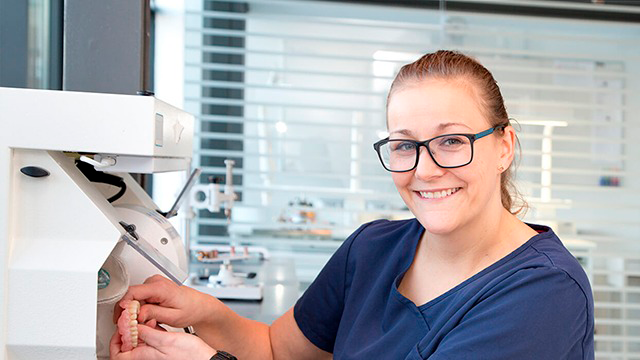 En smilende kvinde i briller arbejder med en tandlæge maskine i et moderne klinikmiljø.