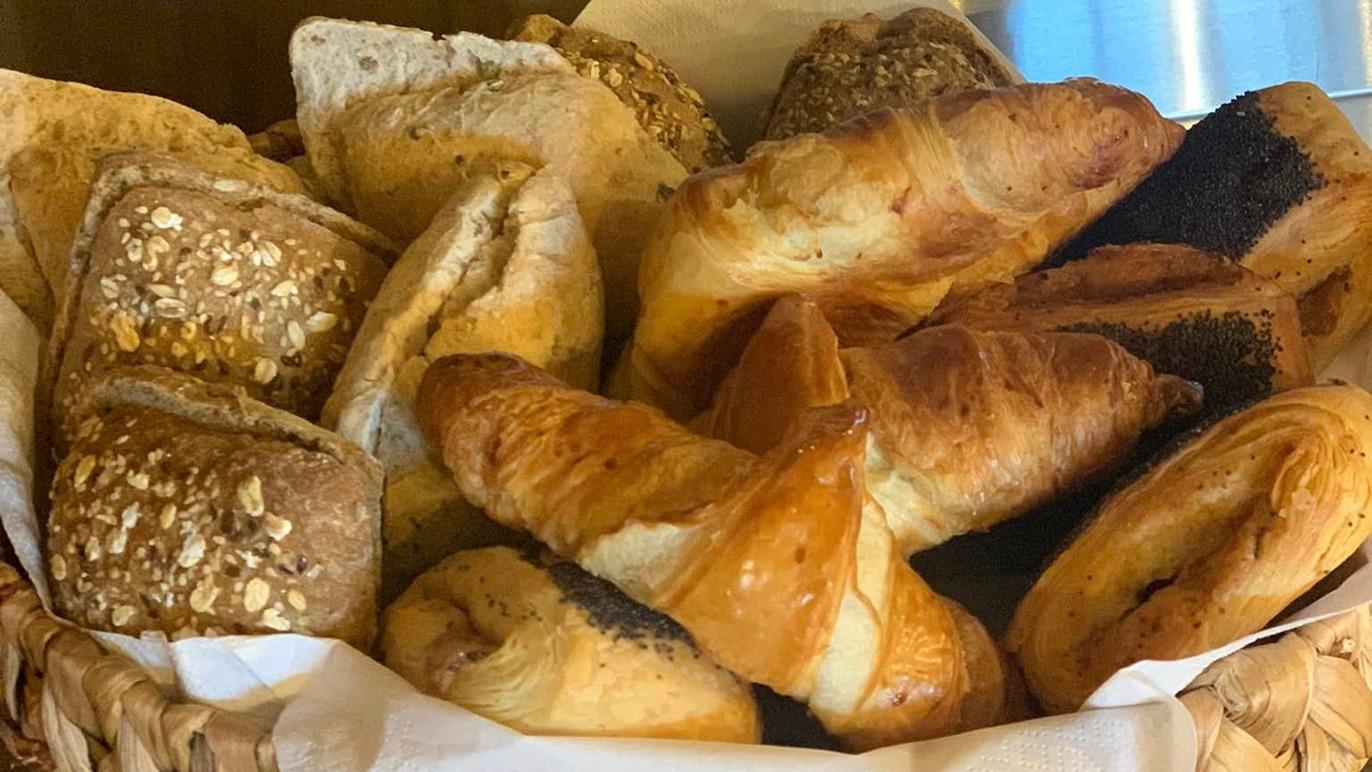 En kurv med forskellige typer brød og bagværk, herunder croissanter, rundstykker og fuldkornsbrød.