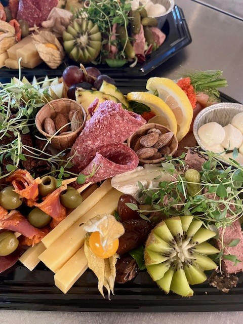 Farverig tapasplade med forskellige oste, pølser, oliven, frugt og nødder præsenteret på en sort tallerken.