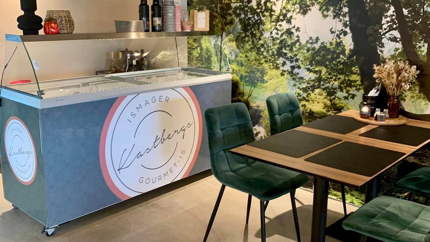 En moderne restaurant med en isdisk og borde i en hyggelig atmosfære, omgivet af en naturvæg.