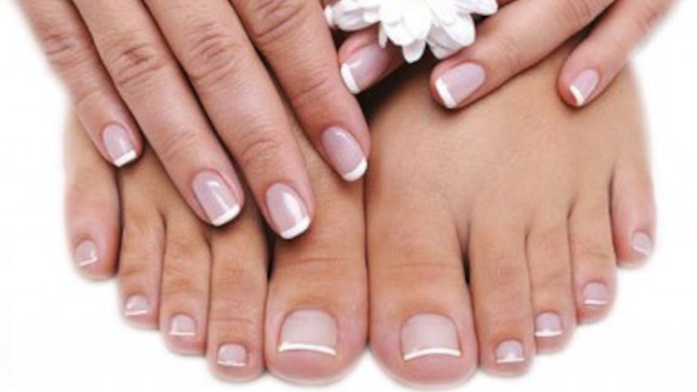 Hænder med fransk manicure og fødder med velplejede negle, prydet med en hvid blomst.