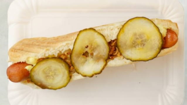 En hotdog med pølser, sprøde løg og skiver af syltede agurker i et brød.