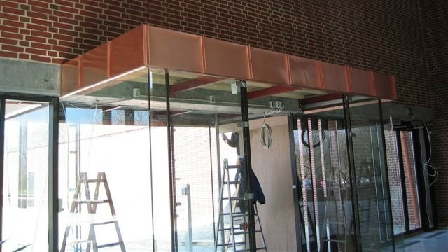 Konstruktion af en glasfacade med kobberoverdækning og stiger i baggrunden.