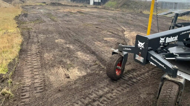 En grusplads med spor fra en maskine og en Bobcat, der står klar til arbejde.