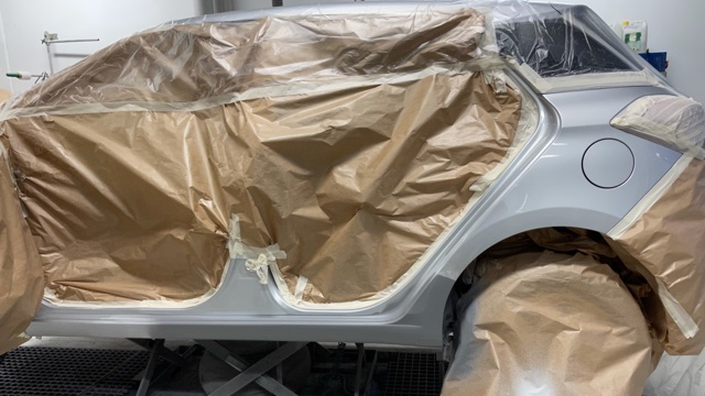 En bil i malerarbejde, dækket med brunt papir og plast, klar til lakering i et malerværksted.