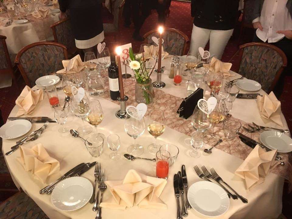 Et elegant dækket middagsbord med vinflaske, glas, servietter og blomsterdekorationer.