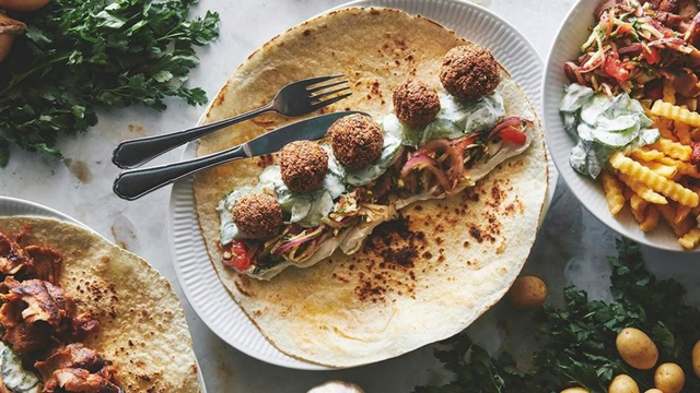 Lækre falafler på en tortilla med salat, tomater og dressing, serveret med pomfritter og salat.