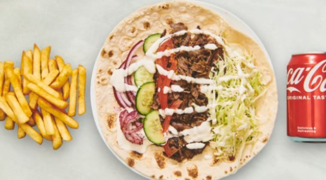 En tallerken med en tortilla fyldt med kød, grøntsager og dressing, serveret med pomfritter og en dåse Coca-Cola.