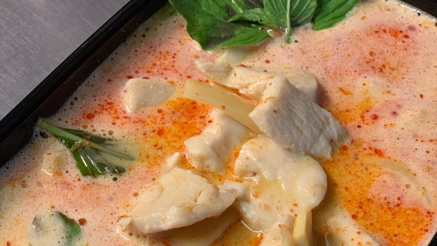 Kyllingesuppe med kokosmælk, friske krydderurter og rød chili, serveret i en sort skål.