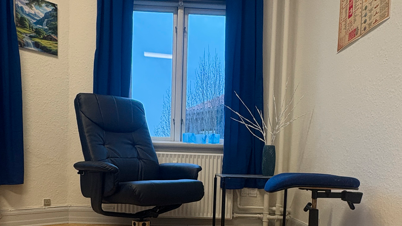 Et lyst rum med en blå lænestol, et lille bord og en vindue med blå gardiner.